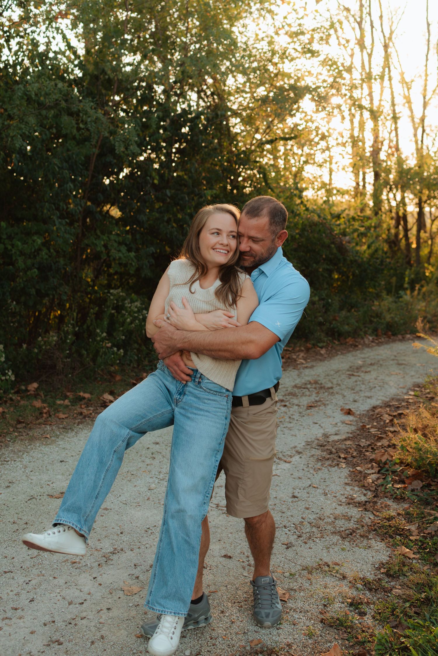 Playful couple embracing and laughing on dirt path during sunset photoshoot.