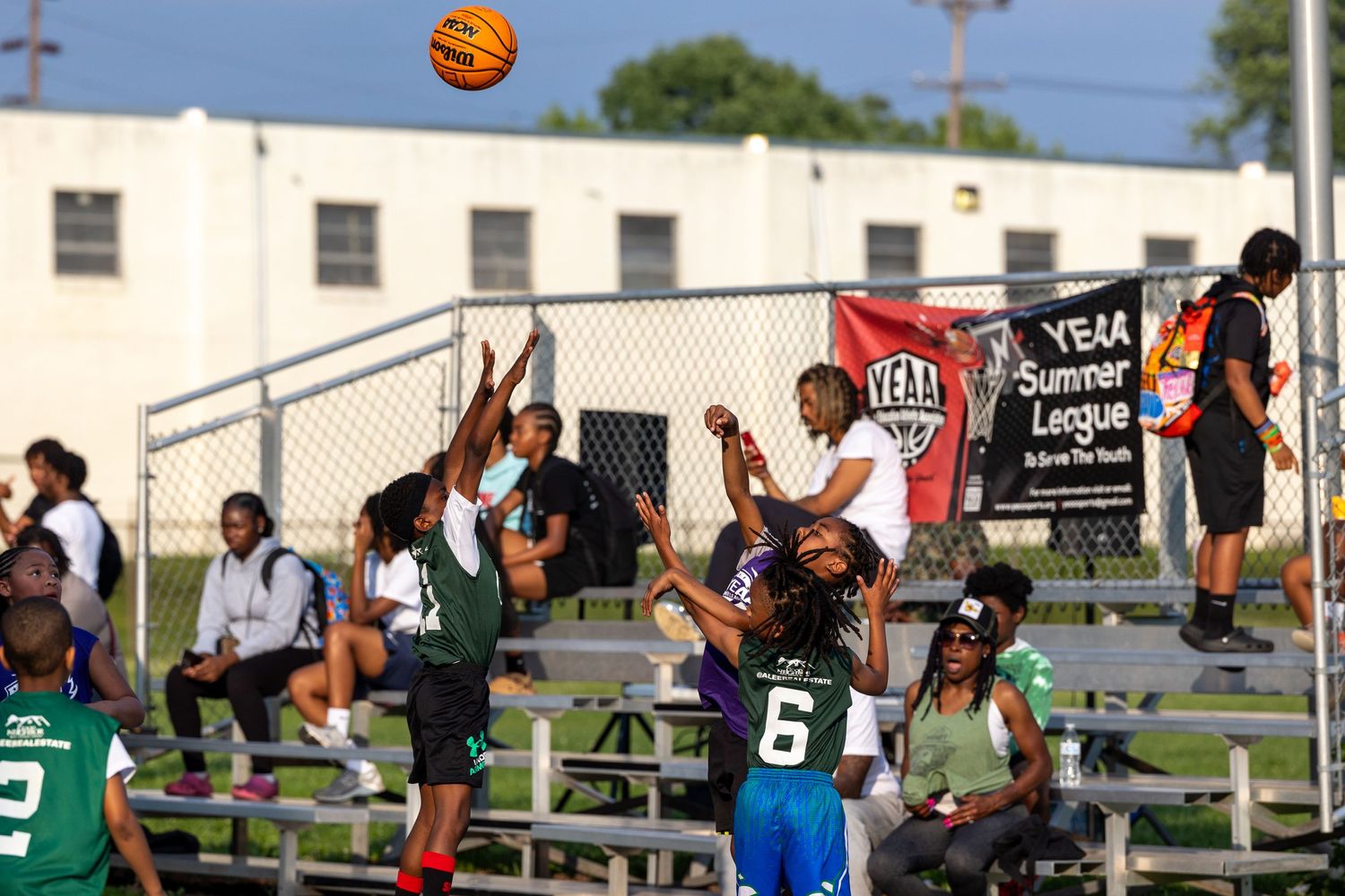 A basketball soars through the air during an outdoor game with players ready to rebound.