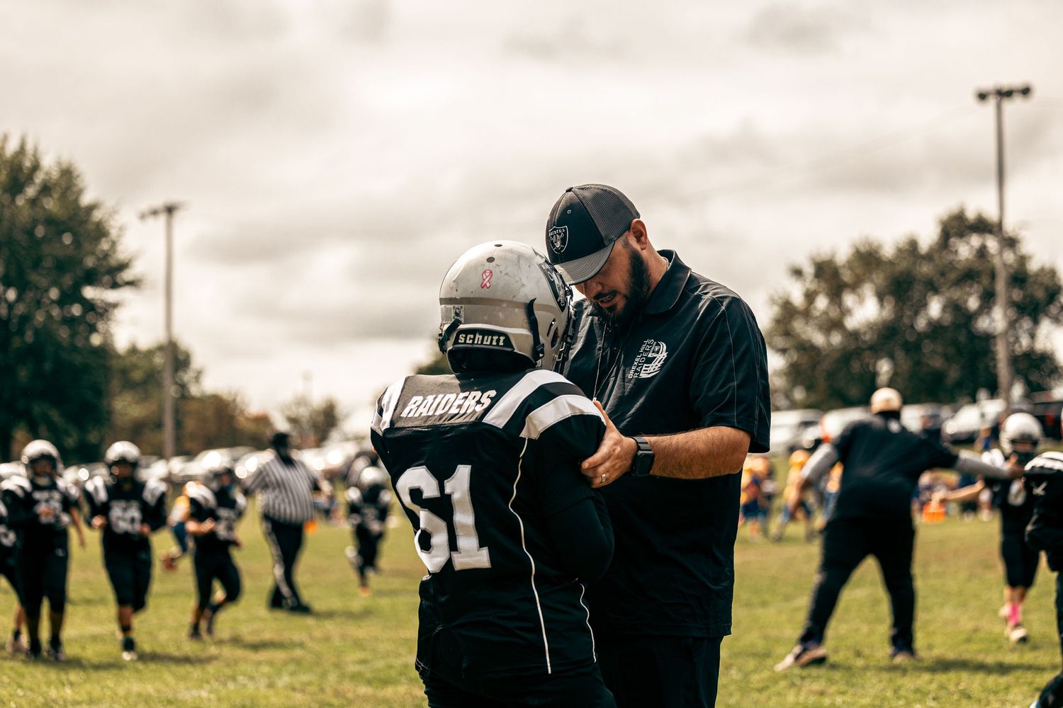 Coach providing guidance to young player in football gear during game.