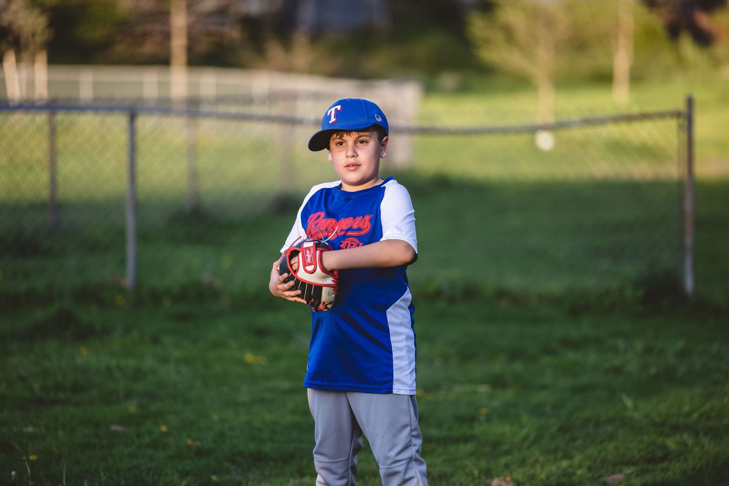 Youth baseball player in blue uniform practicing throwing drills on green grass field.