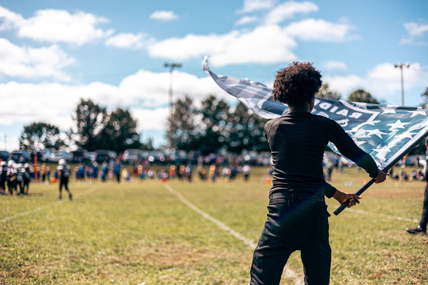 Person in black silhouetted against blue sky performing with color guard flags at sports event.