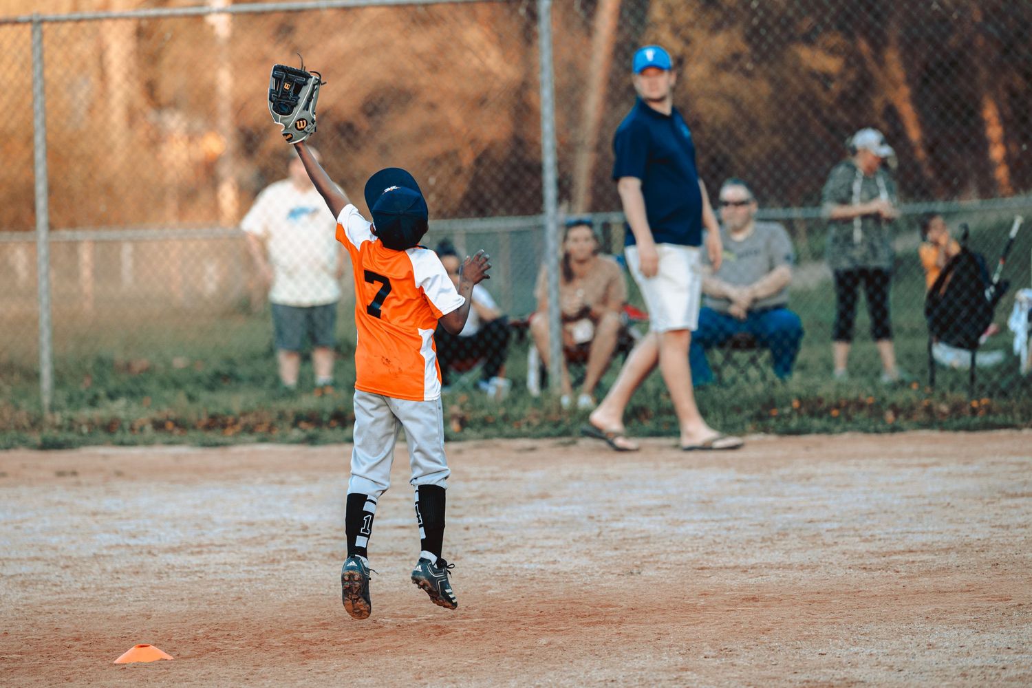 Baseball practice on a dirt field with players in orange jerseys and chain link fence in background.