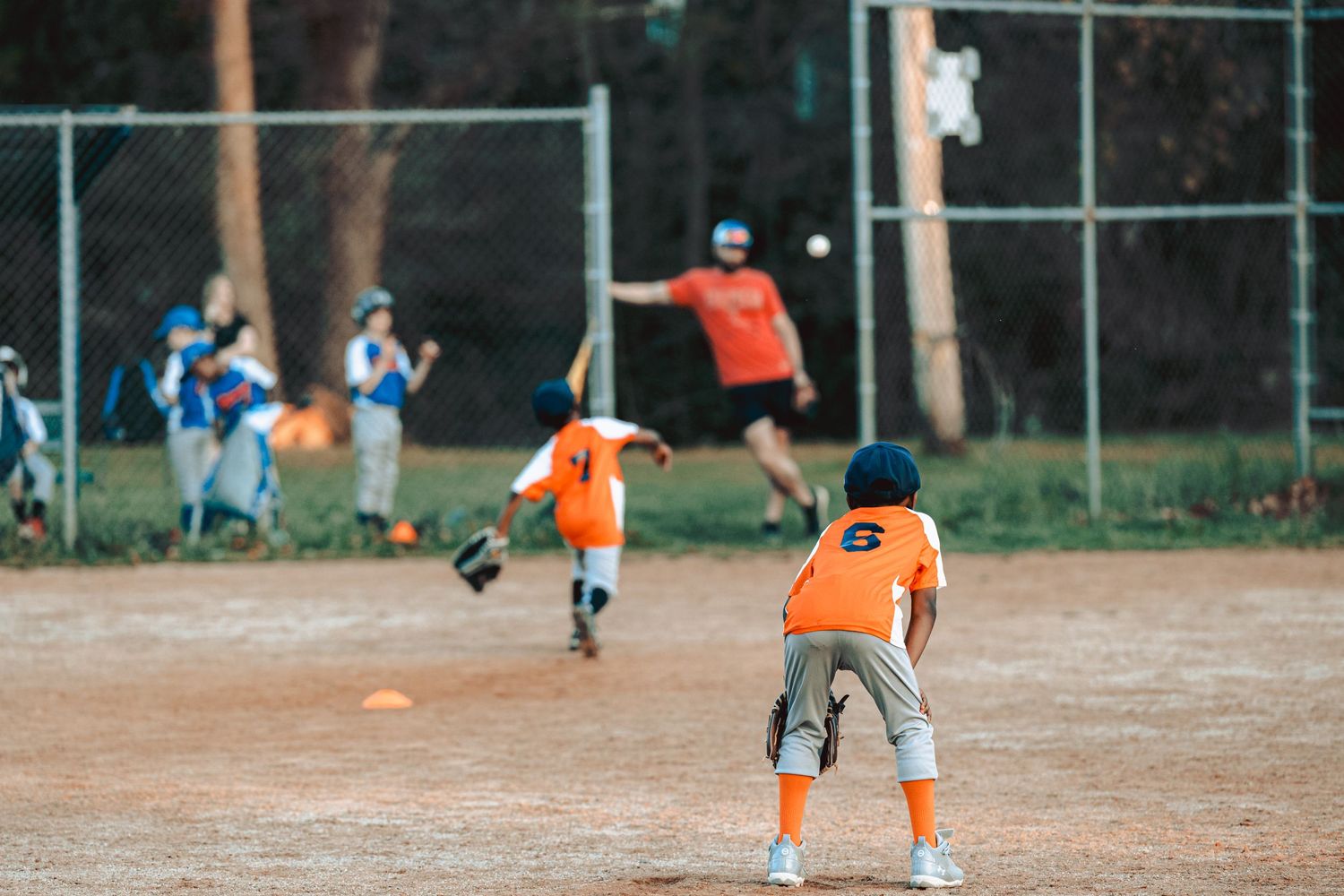 Baseball players on a dirt field with orange uniforms practicing running drills.
