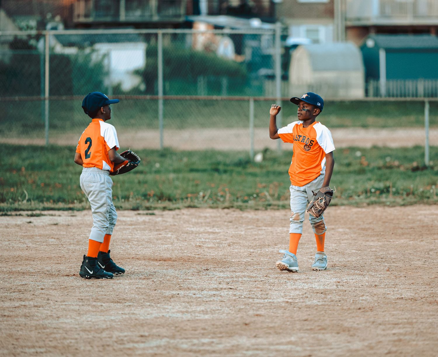 Youth baseball players in orange uniforms practicing fielding drills on a dirt diamond.