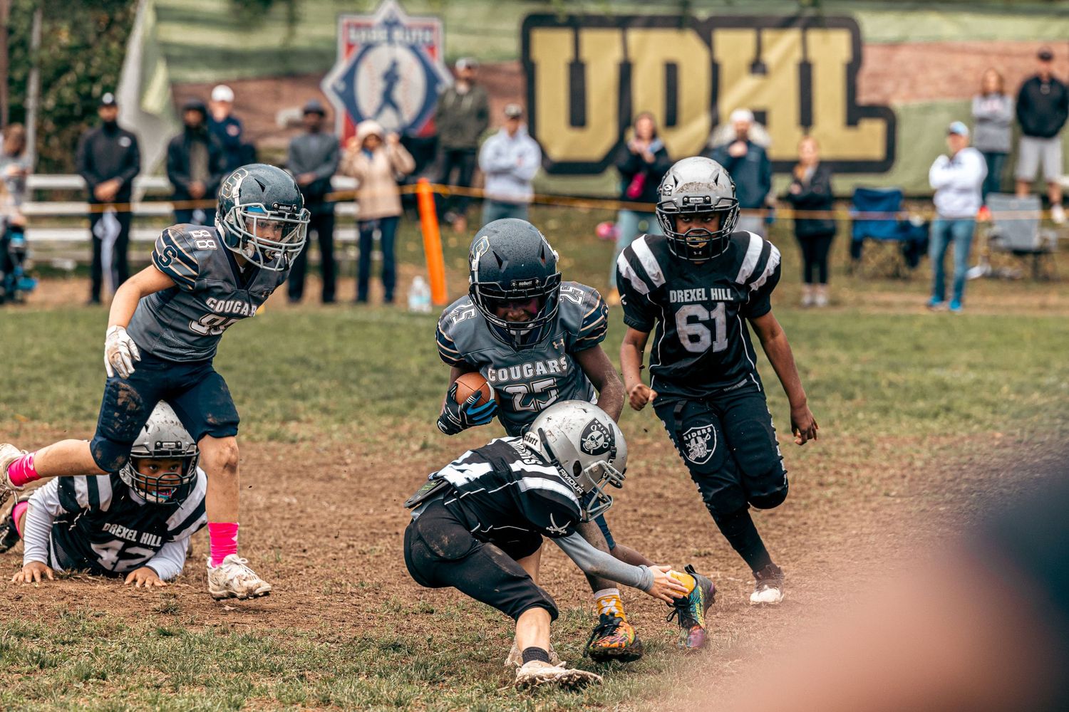 Youth football players in black uniforms making tackles during game play.