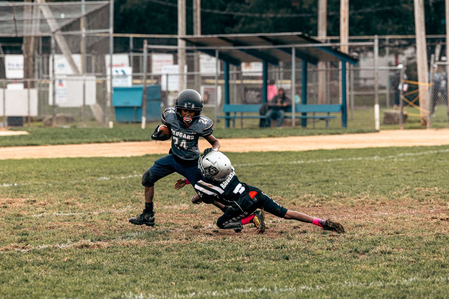 Two youth football players engage in tackling play during game on grass field.