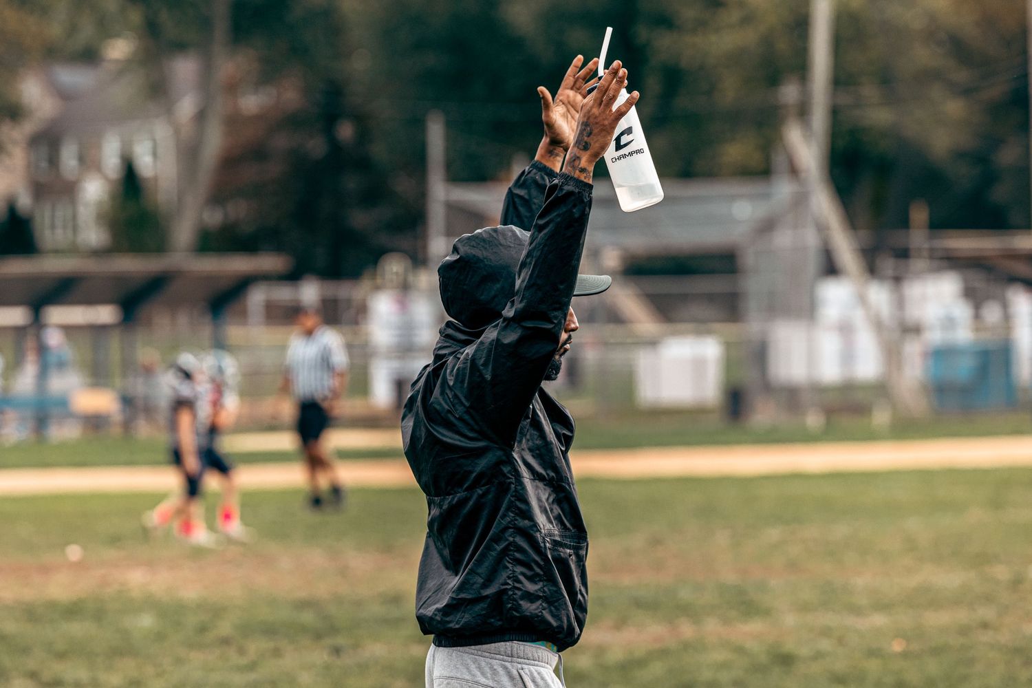 Referee in black jacket signals a call during a youth football game.