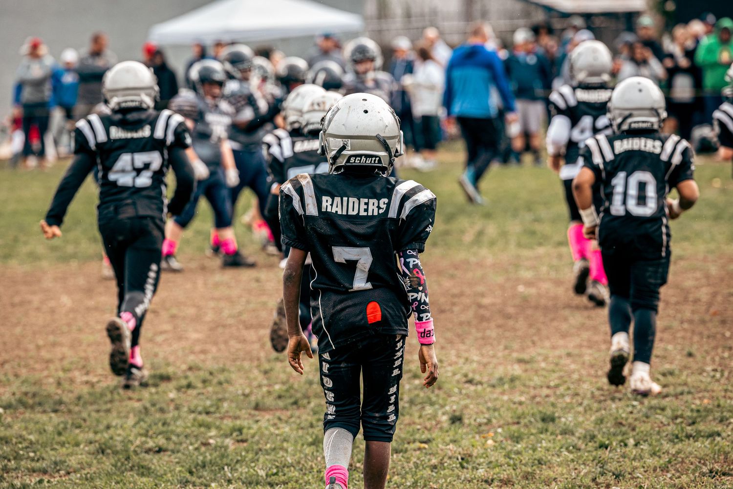 Youth football players in black uniforms with pink accents walking on a field during a game.