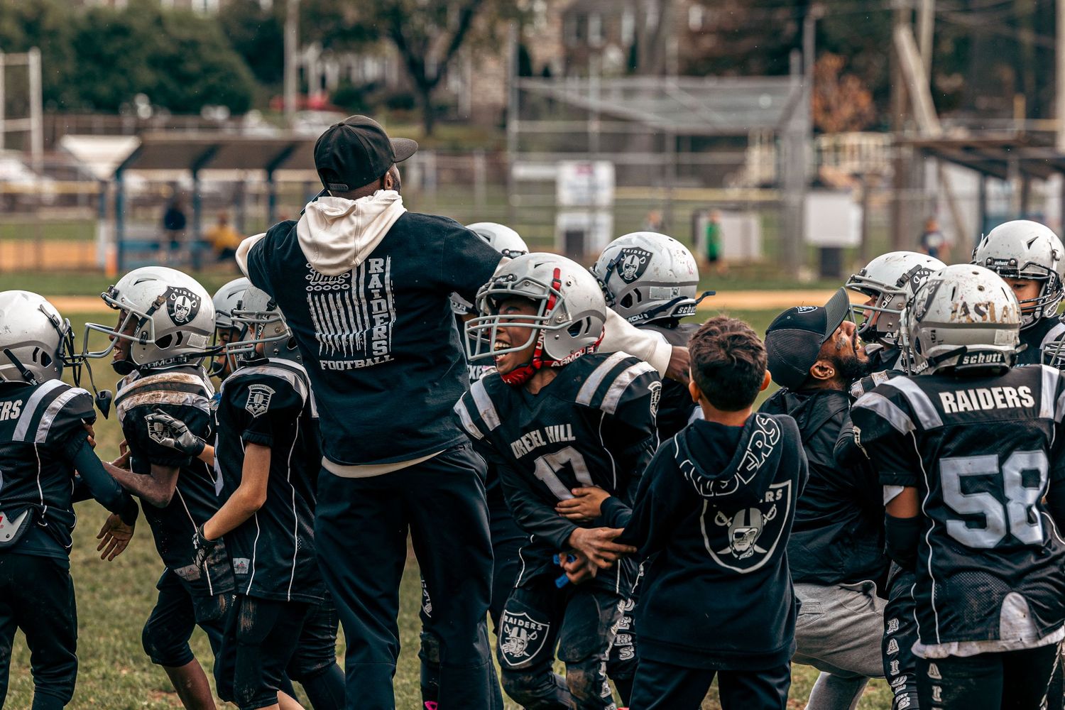 Youth football players in black uniforms line up in formation during a game on a grass field.