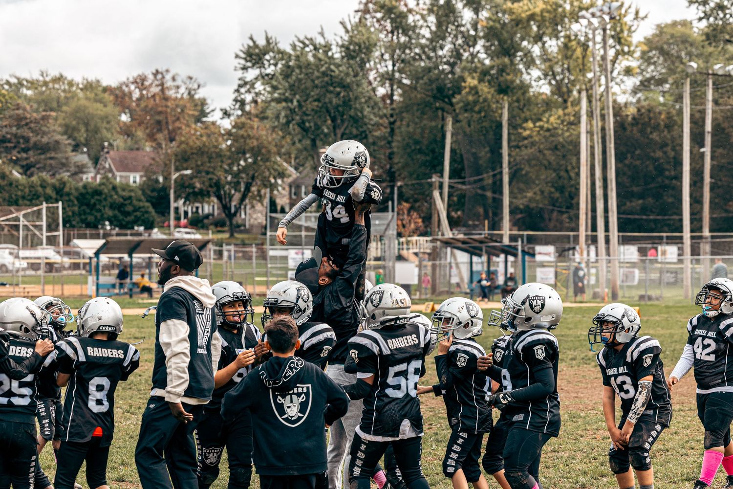 Football team in black uniforms celebrating together on autumn field.