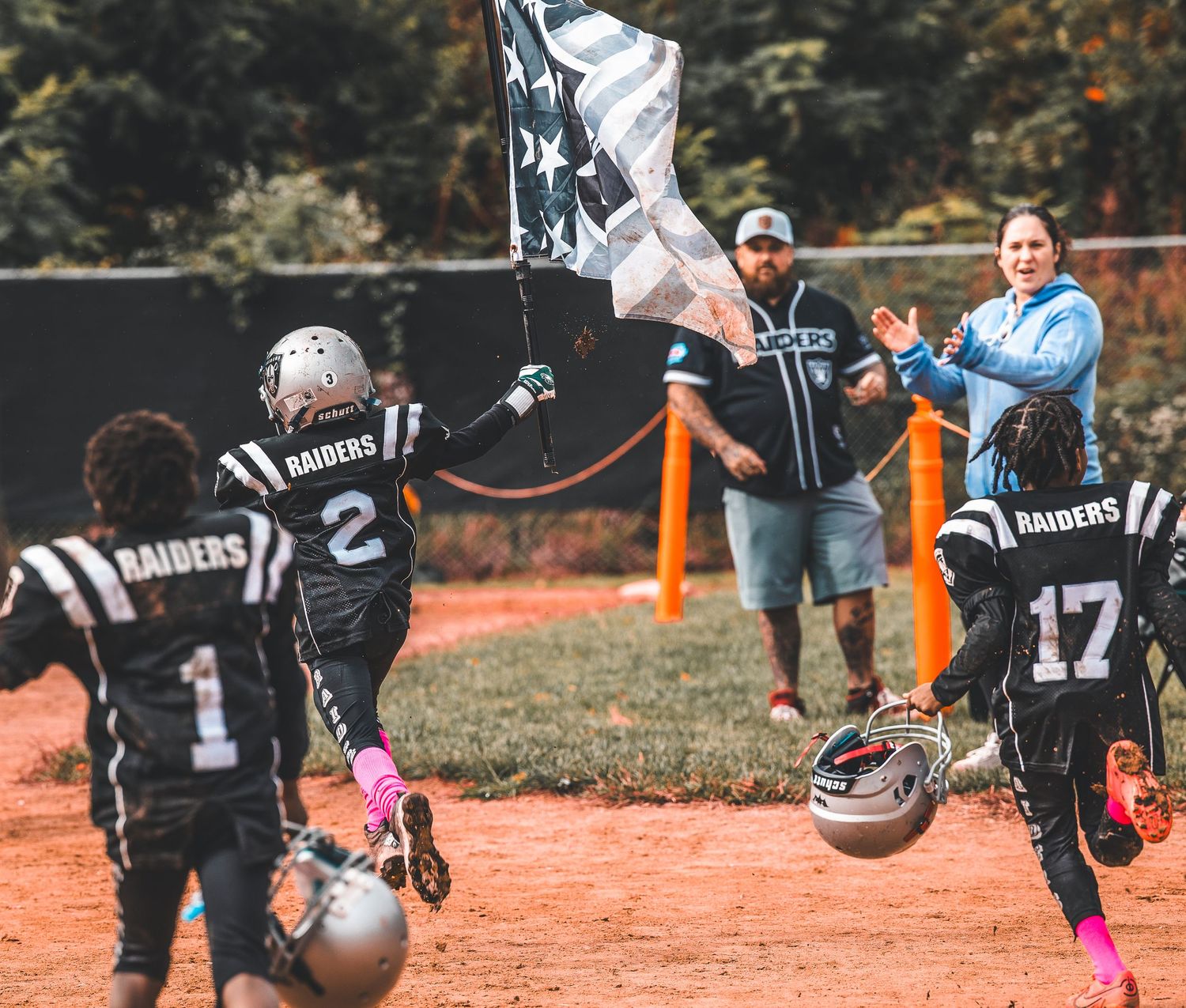 Team of youth football players in black and silver uniforms running together on an outdoor field.