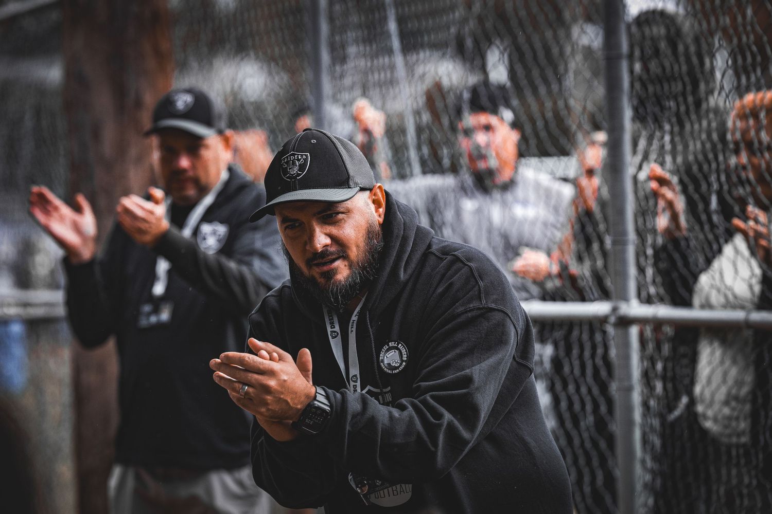 Crowd of spectators cheering and watching from behind a chain-link fence at a sporting event.