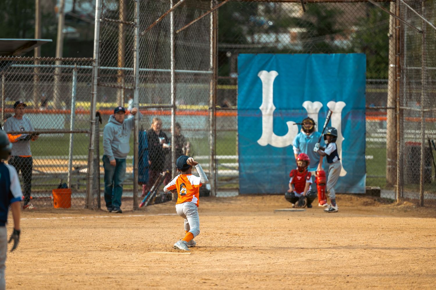 Baseball or softball players practicing on an outdoor field with blue fencing in the background.