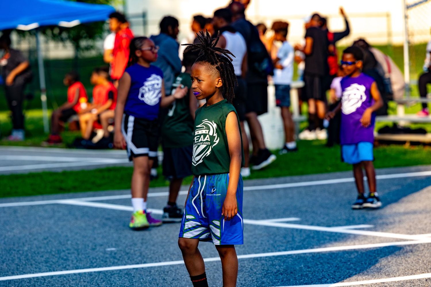 A youth sports event takes place on an outdoor basketball court with spectators watching.