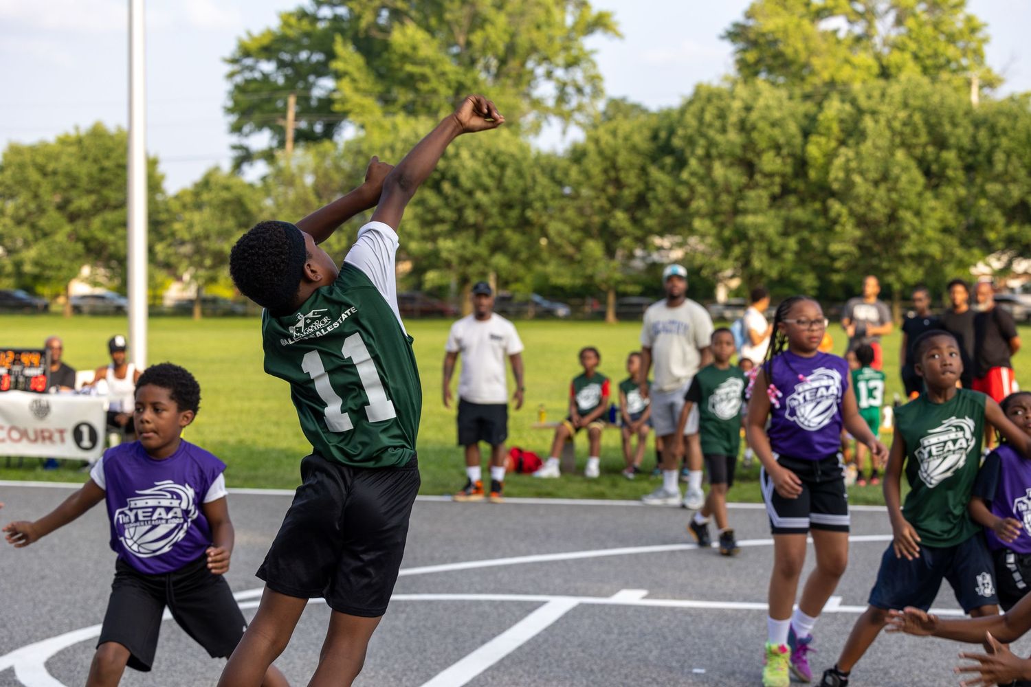 Youth basketball players compete during an outdoor game on a summer day.