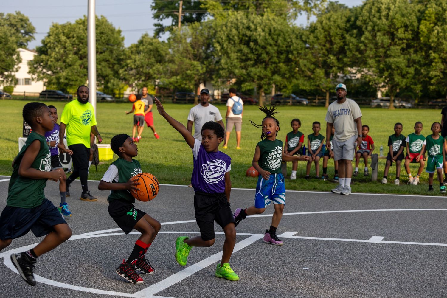 Players practicing basketball drills on an outdoor court with multiple hoops.