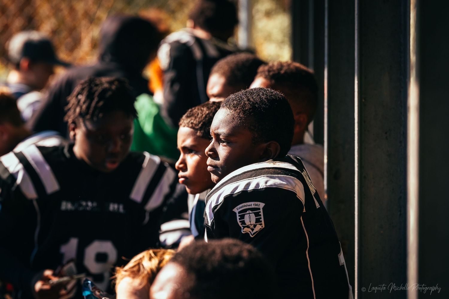 Players watch intently from the sidelines during a youth football game.