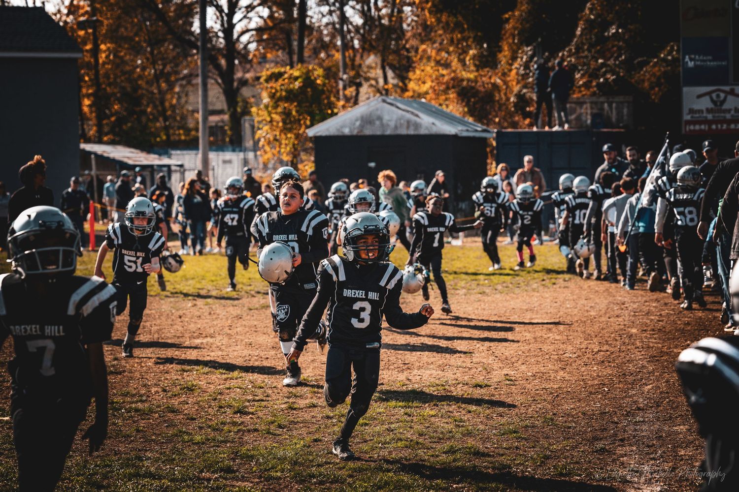 Young football player runs through a tunnel of teammates and spectators on game day.