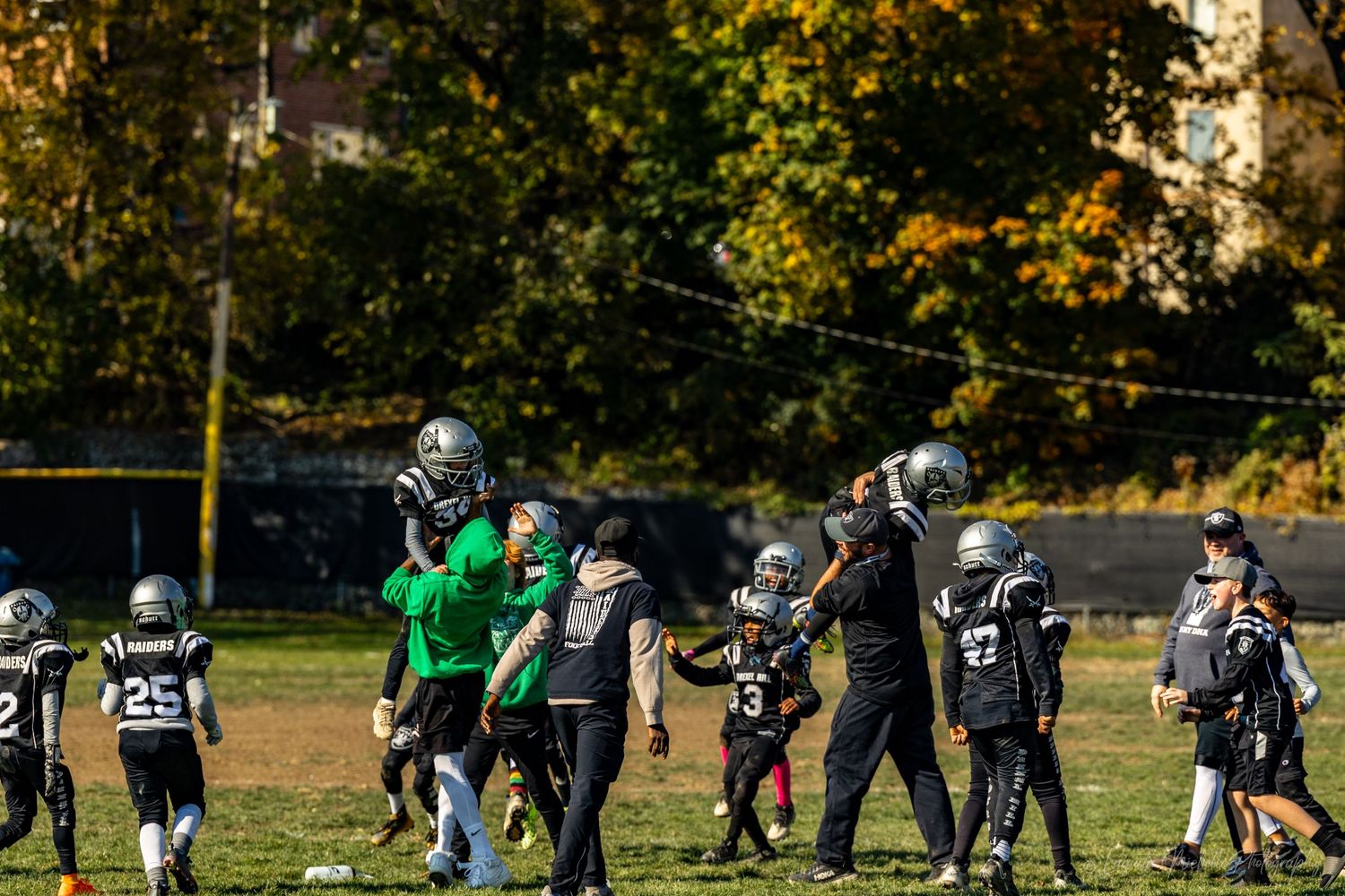 Youth football team practices drills on a field surrounded by autumn trees.
