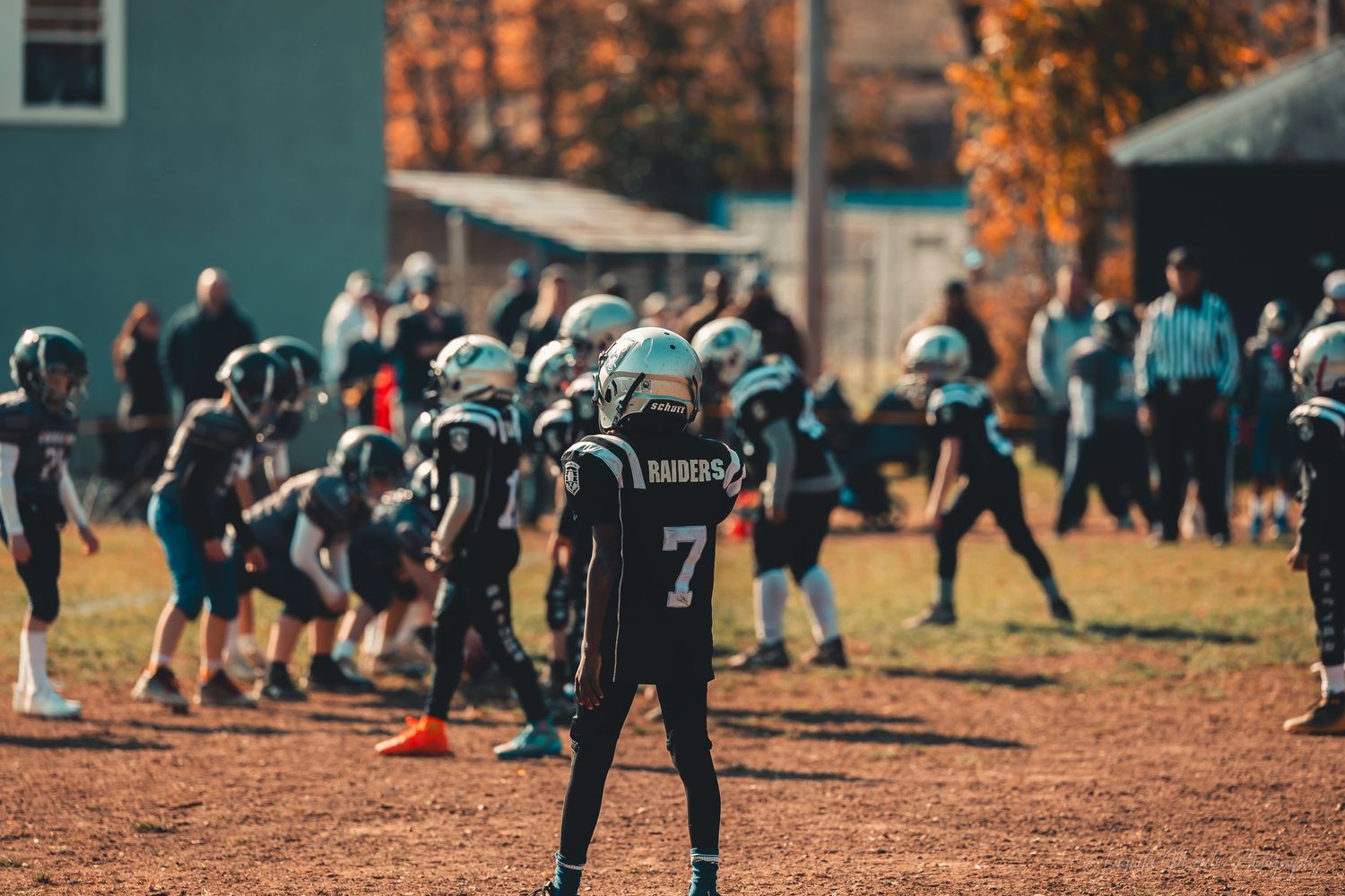 Youth football player wearing jersey number 7 stands ready on autumn sports field.