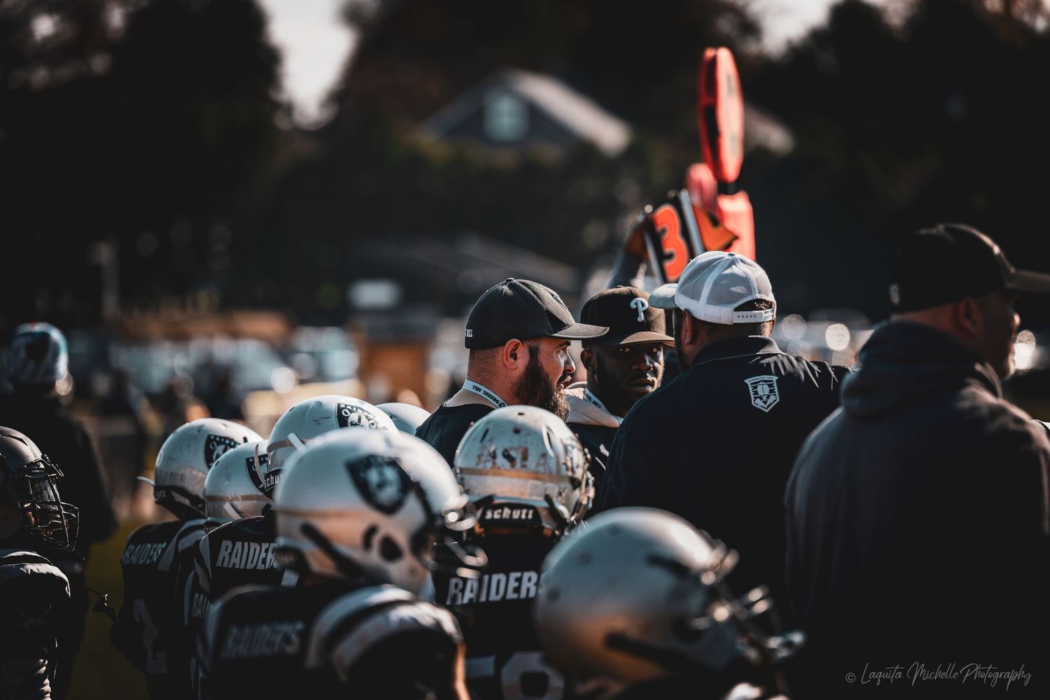 Silhouettes of football players and coaches gathered on the sideline at dusk.