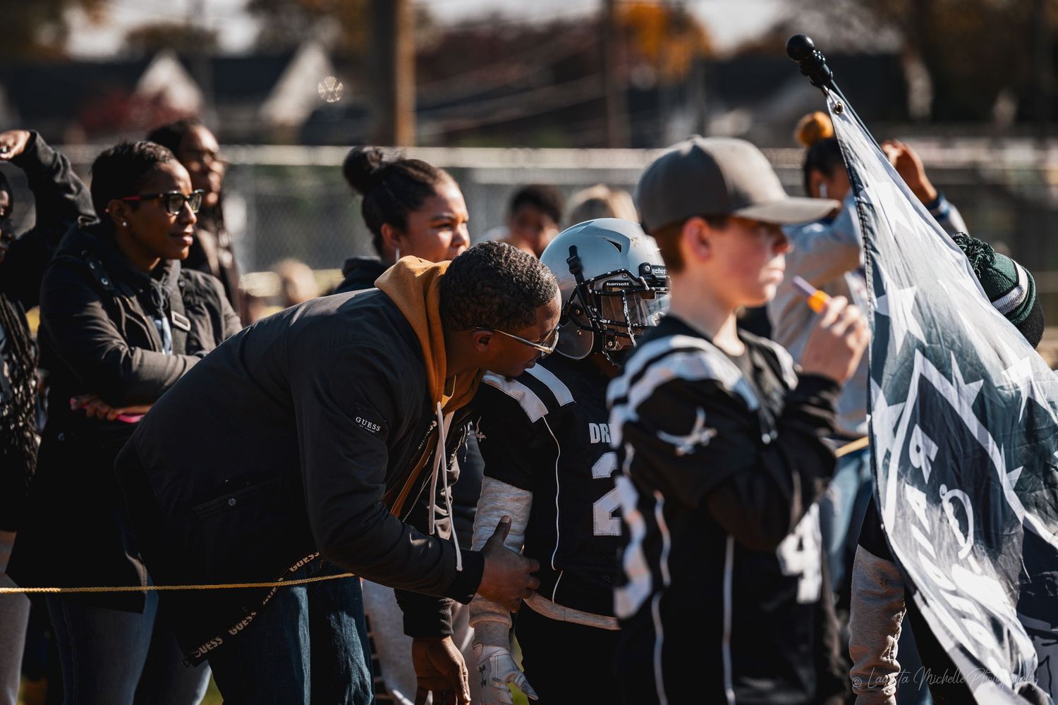Spectators and coaches watching from the sidelines of a youth football game.