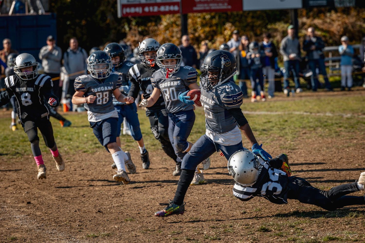 Youth football players line up in formation during an autumn game on a grass field.