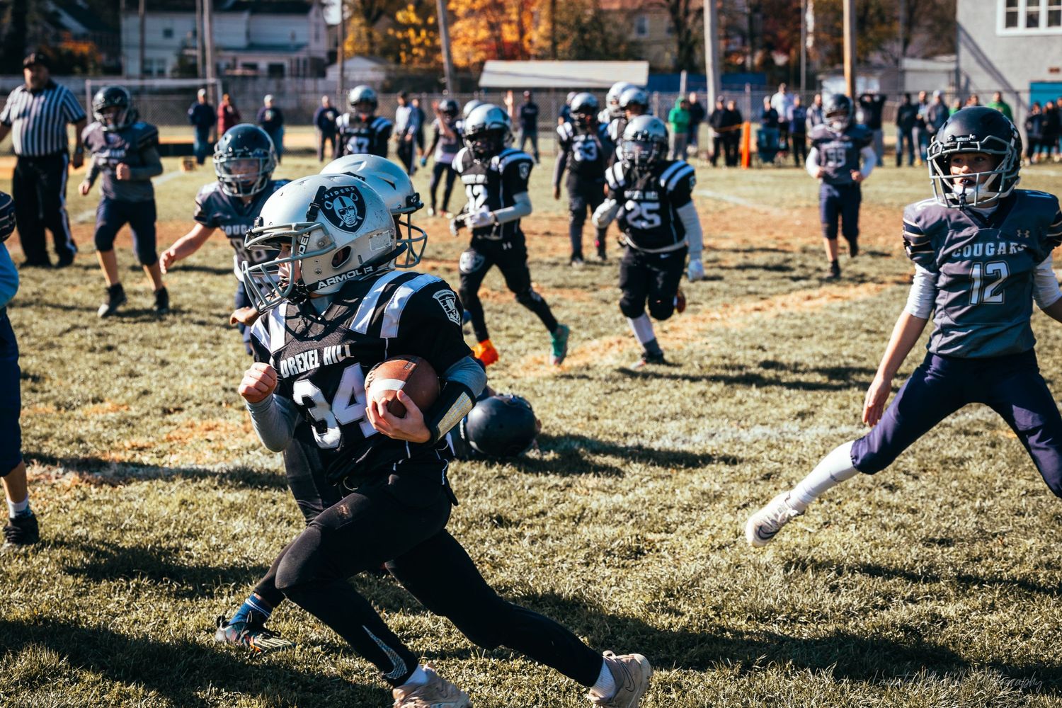 Youth sports practice with players in dark uniforms spread across grass field.