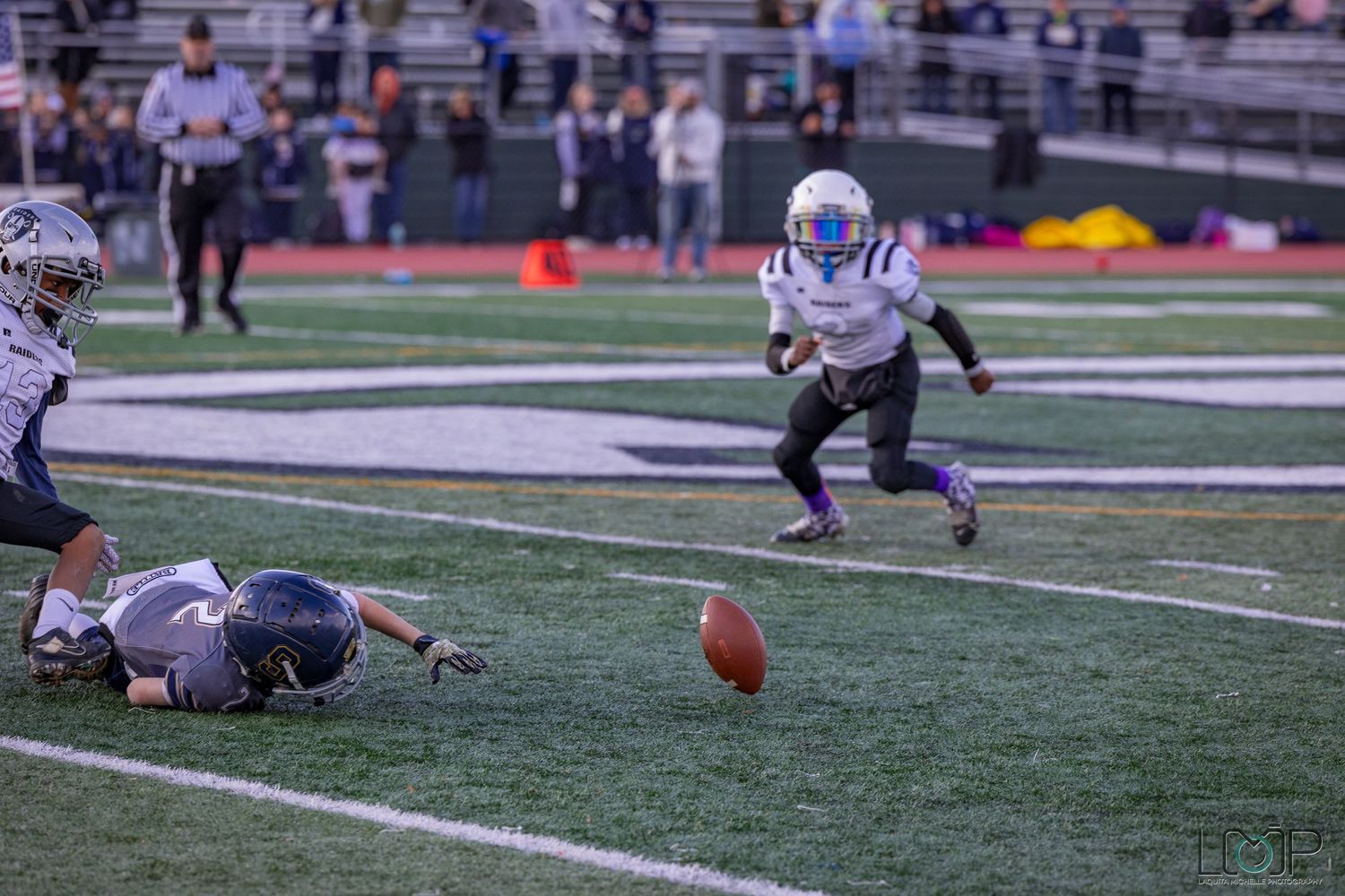Football players diving for loose ball during intense game action on artificial turf.