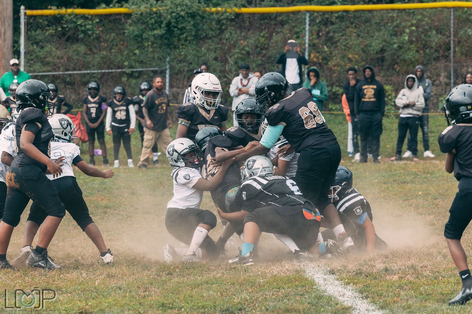 Youth football players creating a cloud of dust during an intense play on the field.