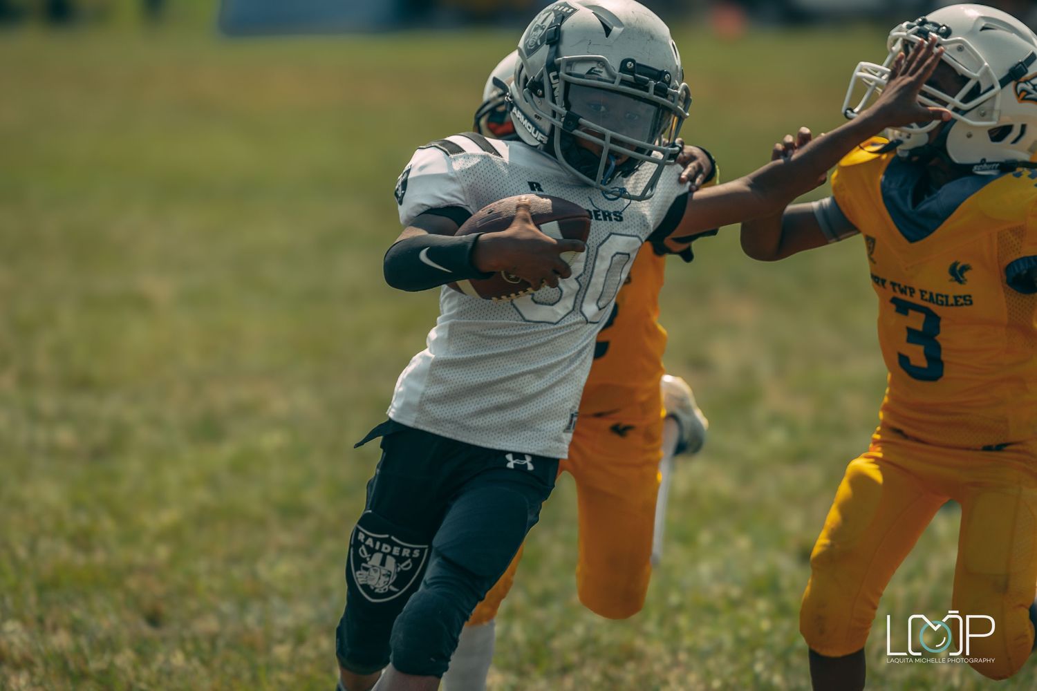 Football player in white jersey carrying ball while opponent in yellow attempts tackle.