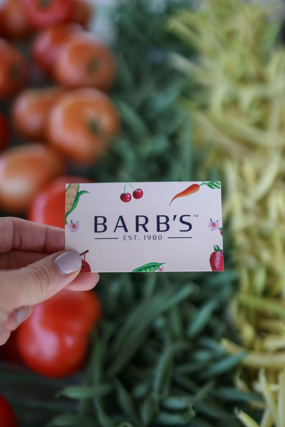 A business card for Barb's held against a background of fresh produce and vegetables.