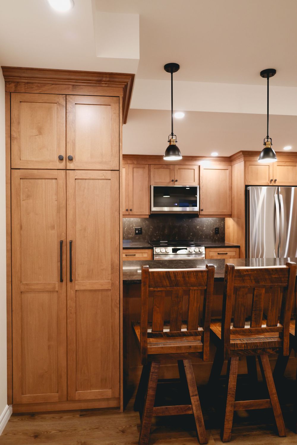 Floor-to-ceiling wooden pantry and cabinetry with bar seating in a modern kitchen.