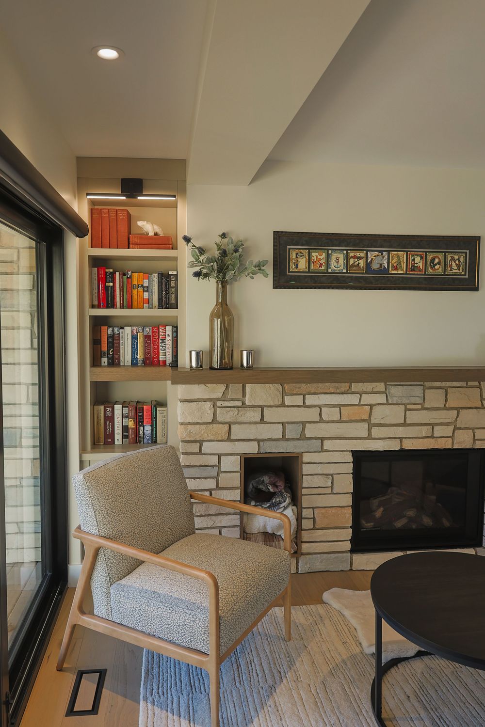 Modern living room corner featuring a gray armchair, stone accent wall, built-in bookshelf and recessed lighting.