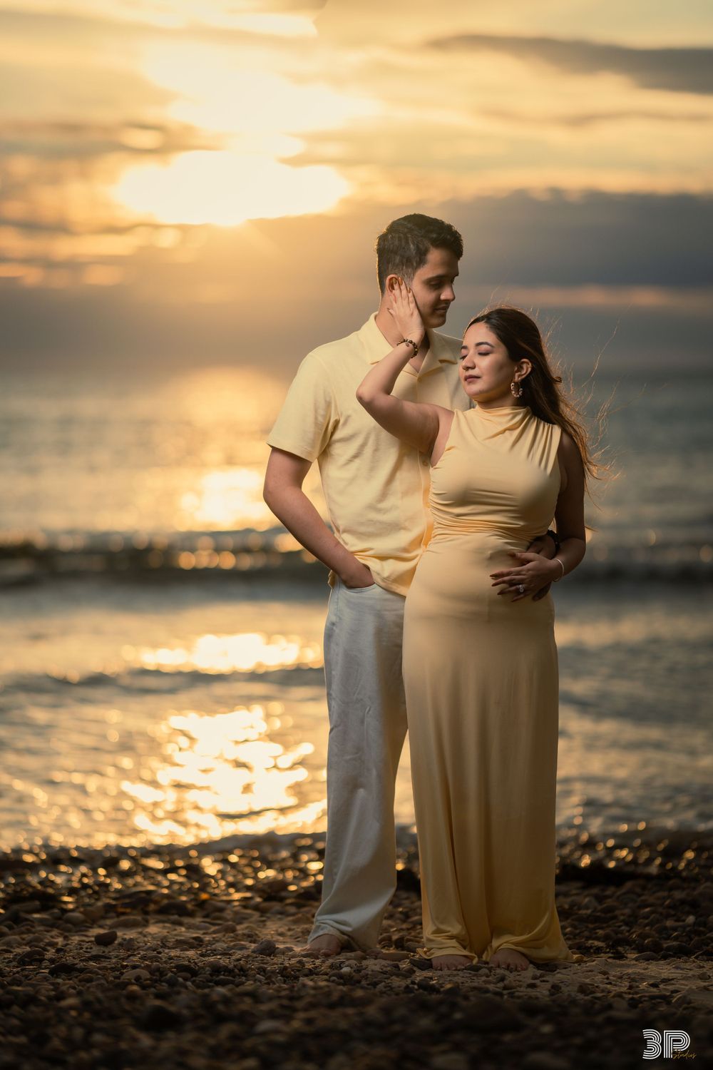 Couple enjoying a beachside pre-wedding photoshoot, captured against the backdrop of the ocean and setting sun.
