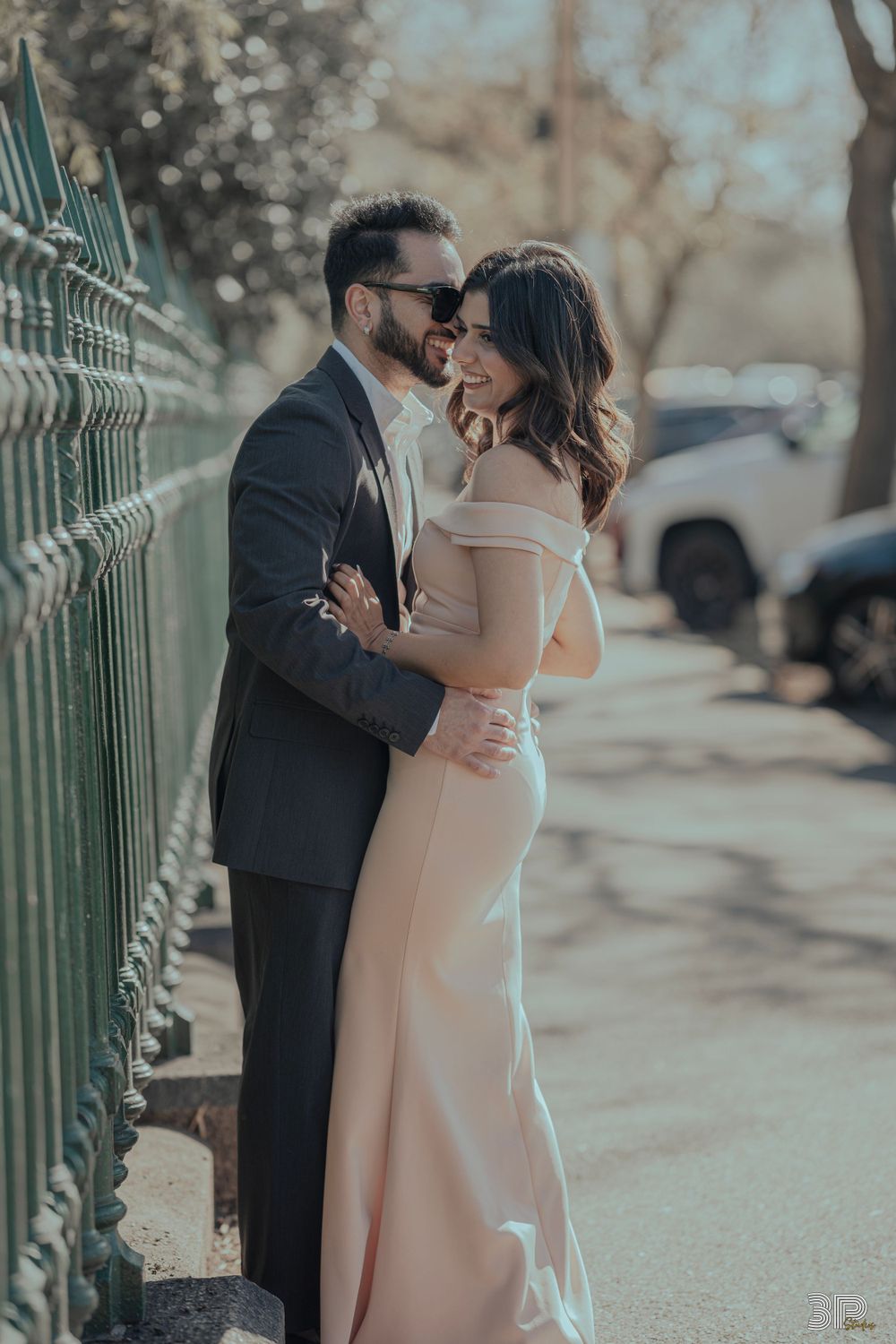 Couple in formal attire embracing against a decorative metal fence.
