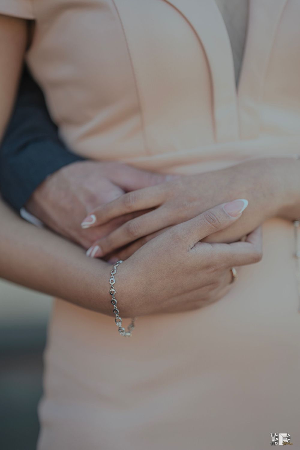 Close-up of hands with engagement ring and delicate bracelet against blush colored dress.