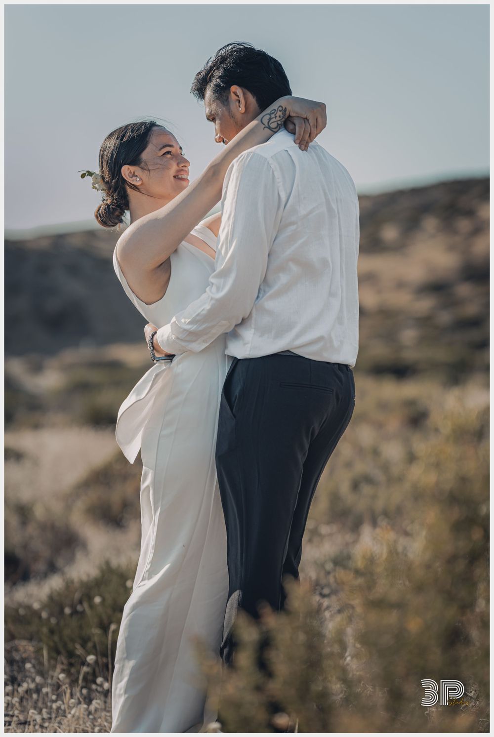 A couple in formal attire shares an intimate moment in a desert landscape.