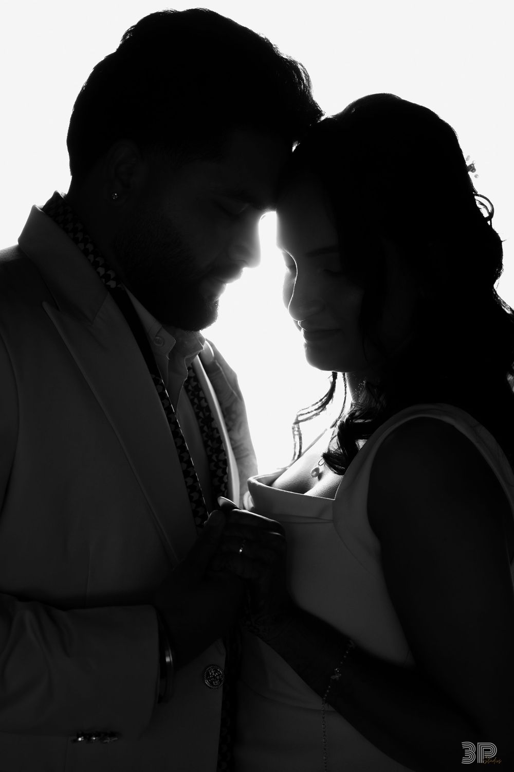 Black and white silhouette of a romantic couple in formal wear touching foreheads in an intimate embrace.