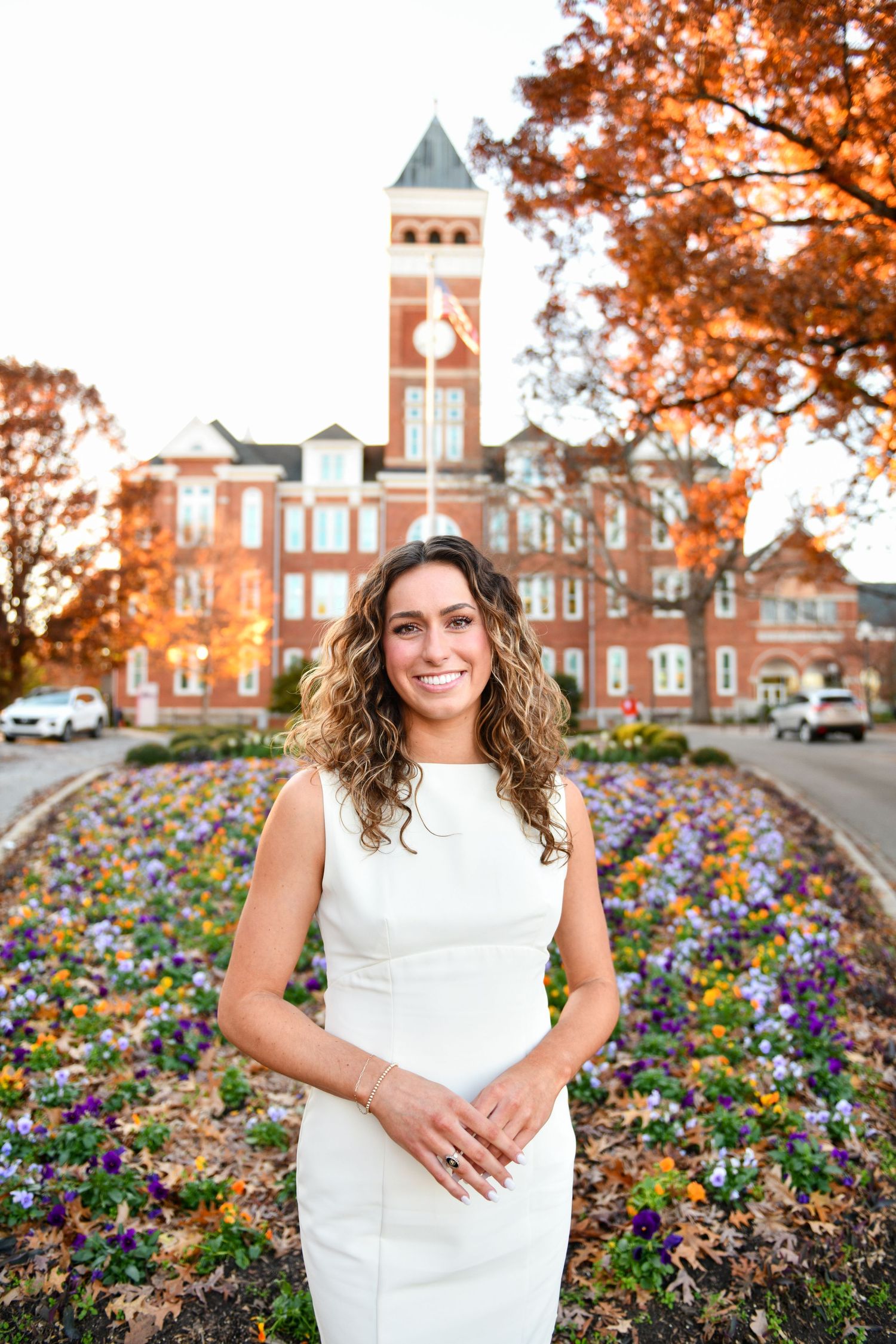 Beautiful campus building with brick clock tower and colorful flower garden in foreground during autumn.