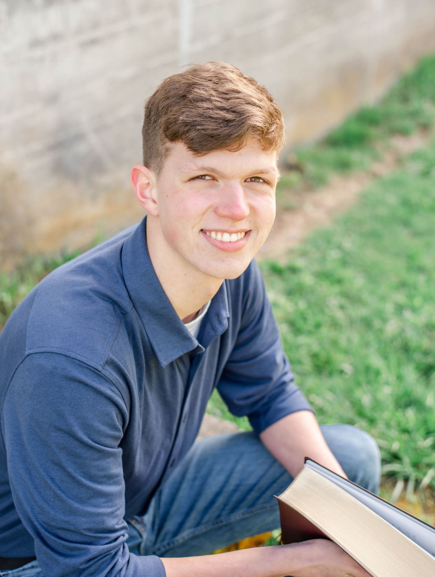 Student in navy polo sits outdoors with book in late afternoon light.