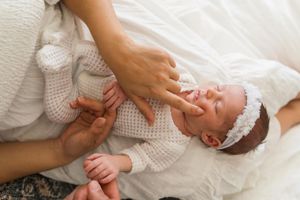 Overhead view of hands gently touching newborn in white knit outfit.