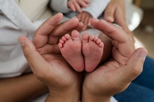 Tiny newborn baby feet being gently cradled in adult hands against a soft white background.