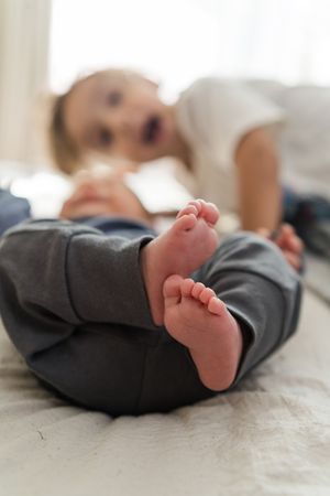 Close-up series of tiny baby feet in gray clothing against white bedding.
