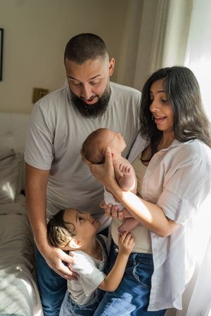 A family shares a tender moment together in a sunlit bedroom, showing affection with their newborn baby.