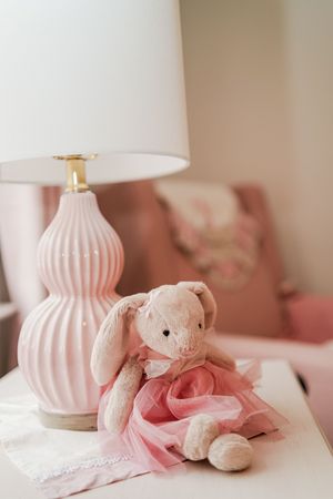 A series of pink nursery decor photos featuring a plush teddy bear and soft pink ceramic lamp on white bedding.