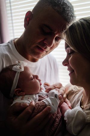 A couple gazes lovingly at their newborn baby in a tender moment captured in soft lighting.