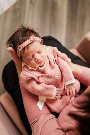 A newborn baby wearing a pink knit sweater rests peacefully in a series of connected photos.
