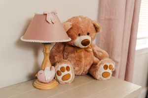 Plush brown teddy bears and pink table lamps decorate a cozy nursery corner with soft curtains and natural lighting.