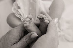 Close-up black and white photo of hands holding a newborn baby's tiny feet.